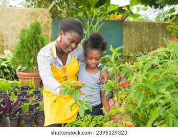 An African Nigerian female woman, mother, florist, entrepreneur, business lady in yellow apron, with a girl child beside her in an Horticulture garden filled with colorful green flowers in Nigeria