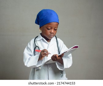 African Nigerian Girl Child With Blue Scarf, Stethoscope And Writing Pad As She Represents Medical Experts Like Doctors, Nurses And Other Medical Practitioners