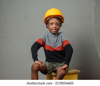 An African Nigerian Girl Child With Yellow Safety Helmet, Sitting While Modeling As A Professional Construction Or Civil Engineer, Architect And Builder Among Others