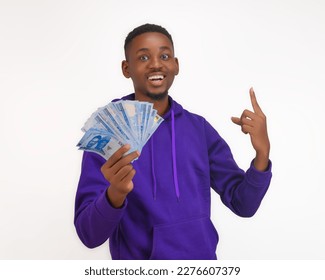 African Nigerian man holding new naira notes smiling happily wearing a purple hoodie pointing finger upwards in direction