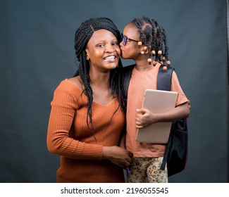 An African Nigerian Mother, Teacher Or Guardian Hugging Her Child Or Daughter While The Girl Kisses Her On The Cheek And Also Holding An Education Smart Tablet