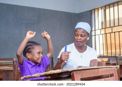 African Nigerian Mother Or Teacher Sitting Together With Her Girl Child In A Classroom, Helping Her With Her Studies Towards Excellence In Her, School, Education And Career