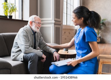 African nurse in uniform talking during day visit to old patient grandfather. Caring caregiver hold hand of 80s senior elderly man people having pleasant conversation, satisfied grandfather receiving.