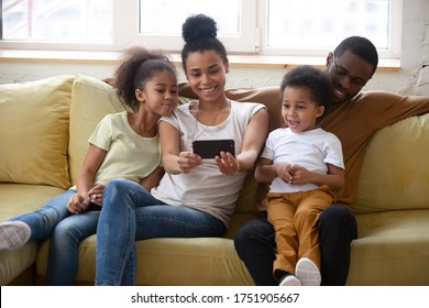 African parents and little adorable kids sitting on sofa in cozy modern living room having fun make selfie using smart phone. Chatting with relatives via videocall, modern tech family weekend concept - Powered by Shutterstock