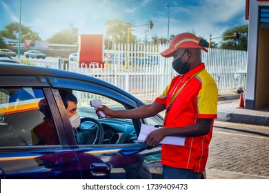 African Petrol Attendant Checking Temperature Of The Driver With An Infrared Thermometer At A Gas Station In Botswana