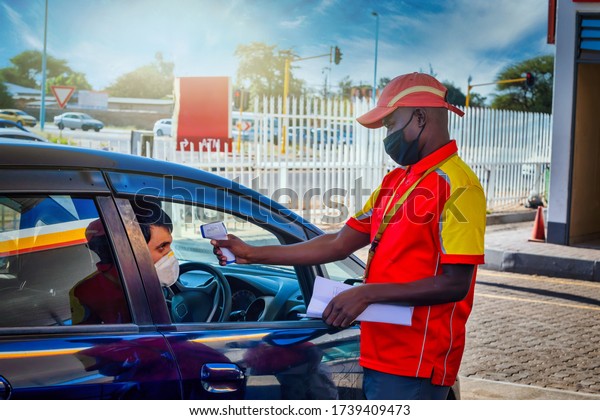 African\
petrol attendant checking temperature of the driver with an\
infrared thermometer at a gas station in\
Botswana