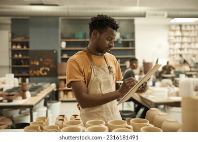 African pottery studio manager taking inventory in a workshop - Powered by Shutterstock