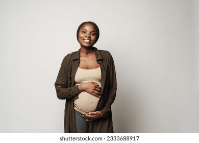 African pregnant happyyoung woman standing and holding her belly looking in camera over isolated brown background - Powered by Shutterstock