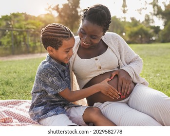 African Pregnant Mother And Mixed Race Son Touching Belly At City Park - Family Love