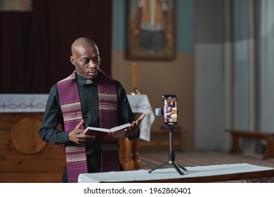 African priest holding Bible and performing during live broadcast on mobile phone online