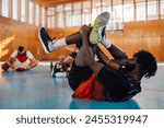 African professional basketball team player stretching and warming up before training in a sports hall. Health, wellness and game start. Black man in sports outfit warming up on the floor. Copy space.