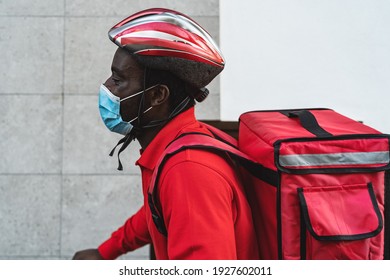 African rider man delivering meal to customers with electric bicycle while wearing face mask during corona virus outbreak - Eco fast delivery food concept - Powered by Shutterstock