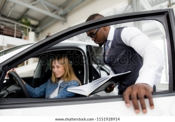 African sales consultant shows the girl the\
salon of a new car in the\
showroom