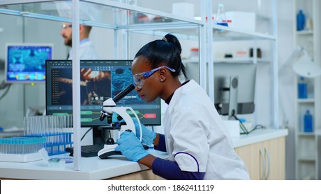 African Scientist Checking Sample Of Virus Using Microscope In Modern Lab. Multiethnic Team Examining Vaccine Evolution Using High Tech For Scientific Research Of Treatment Development Against Covid19