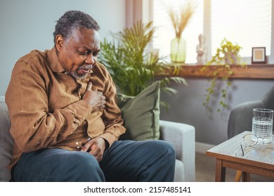 African senior man sitting on sofa at home with sickness. Elderly male suffering from heart attack and feel unwell need for medicine. Retirement people health care and illness recovery concept - Powered by Shutterstock