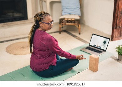 African senior woman doing yoga at home with laptop - Meditation, mindfulness and health care concept