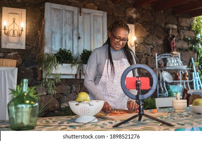 African senior woman streaming online virtual masterclass cooking lesson outdoors at home - Focus on face 