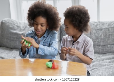 African siblings sit on couch spend time using play dough making diverse shapes have fun together at home, older sister teach younger brother to create. Hobby pastime useful activities for kid concept - Powered by Shutterstock