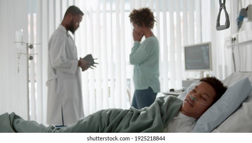 African sick kid sleeping in hospital bed with doctor telling mother bad news on background. Pediatrician consulting crying woman about ill son diagnosis and treatment in hospital ward - Powered by Shutterstock