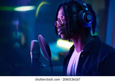 African singer with dreadlocks singing to microphone and recording a song the recording studio - Powered by Shutterstock