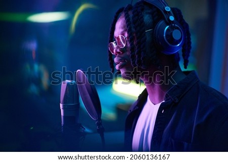 African singer with dreadlocks singing to microphone and recording a song the recording studio
