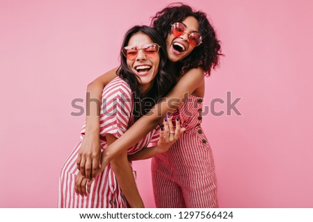African sisters with dark curls are having fun in wonderful mood. Portrait of embracing girls with beautiful appearance