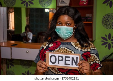 An African Small Business Owner, Makeup Artist, Holding A Open Sign In Her Store