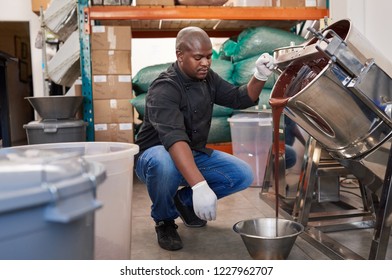 African small business owner pouring melted chocolate from a mixer into a container while working in an artisanal chocolate making factory  - Powered by Shutterstock