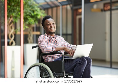 African smiling man sitting in wheelchair and using laptop computer in the mall - Powered by Shutterstock