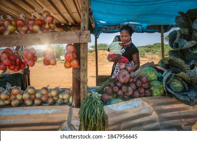 african street vendor, mother holding her child between the bags of cabbage and tomatoes in the shed