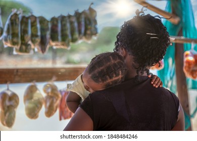 African Street Vendor, Mother Holding Her Child Between The Bags Of Peppers And Tomatoes In The Shed