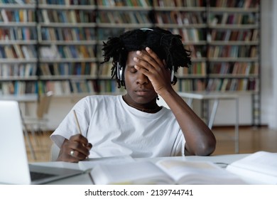 African student feels tired due to long preparations for college exam, deadline task, suffers from headache sit at table with laptop in library. Information overload during admission, stress concept - Shutterstock ID 2139744741