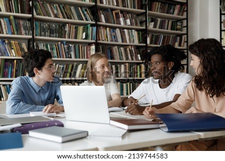 African student guy with schoolmates sit at table in library discuss collaborative task. Multi ethnic schoolgirls schoolboys learn subject, studying together, gain knowledge, prepare for exams concept