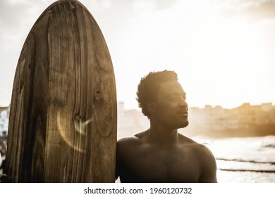 African surfer man holding vintage surf board on the beach at sunset - Soft focus on face - Powered by Shutterstock