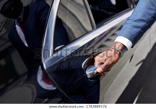 african\
taxi driver opening the door of car, help female client to get out\
of car. in luxurious executive car, business\
lady