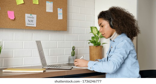 African Teen Girl School College Student Remote Worker Wear Headphones Learn Watch Online Webinar Webcast Class On Laptop Pc Elearning Writing Notes Or Video Calling Working Studying From Home Office.