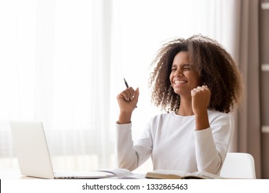 African teen schoolgirl sitting at desk learning studying use pc training materials received great news highest mark successfully pass exams or test at school, accomplish homework feels happy excited