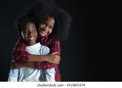 African Teen Siblings Boy And Girl Hugging With Smiley Face On Black Background. Older Sister Back Hug Her Brother. Good Family Relationship Concept