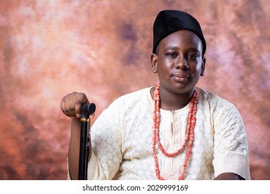 African Teenage boy wearing traditional outfit holding a walking stick with an abstract background