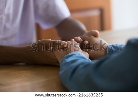 African teenage dating couple having serious talk, sitting at table, holding hands. Loving parent giving sympathy, help, psychological support to kid. Arms close up, cropped shot 商業照片 © 