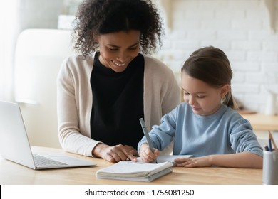 African Tutor Engaged With Schoolgirl Help Complete Tasks Seated At Table At Home. Concept Of Education Kid Development, European Child Homeschooling Writing Homework With American Stepmother Concept