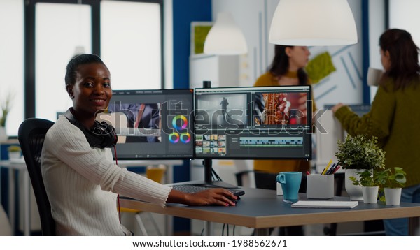 African video editor looking at camera smiling
editing video project in post production software working in
creative studio office. Videographer editing audio film montage on
professional computer