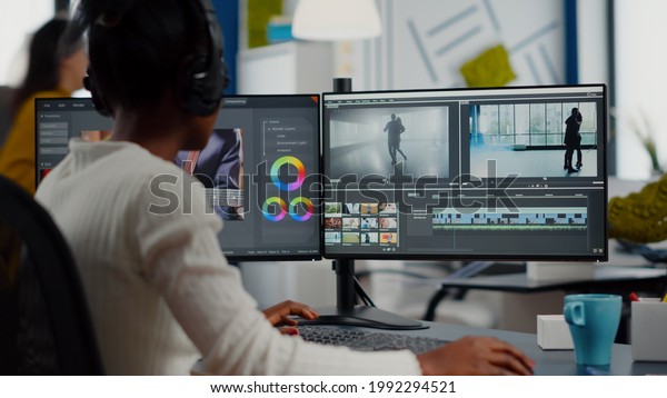 African video editor working with footage and
sound, editing new project cutting film montage sitting in modern
agency office. Woman using computer processing movie in post
production software