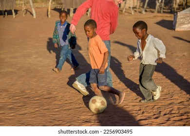 African village children playing football on the dirt in the yard with a Caucasian young adult  - Powered by Shutterstock