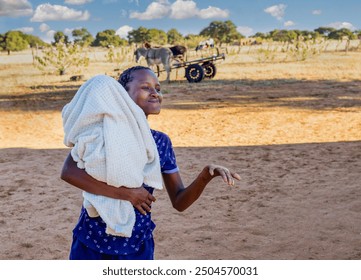 african village life, young girl holding a baby, wearing braided hair, donkey cart in the background - Powered by Shutterstock