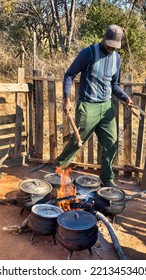 African Village Man Preparing Slow Cooking Food On The Side Of The Road In Cast Iron Pots