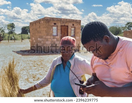 african village, old woman opening in front of the house with an ngo worker on the phone
