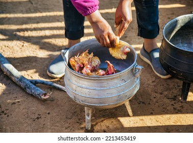 African Village Woman Preparing Chicken On The Side Of The Road In Cast Iron Pots