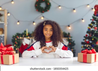 African vlogger girl doing a loving heart gesture while making video, thanking subscribers and followers for support, promoting charity on social media and wishing Merry Christmas and Happy New Year - Powered by Shutterstock