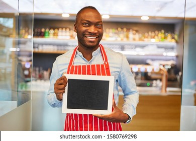 African Waiter Holds Empty Signboard In Front Of Bar Or Restaurant